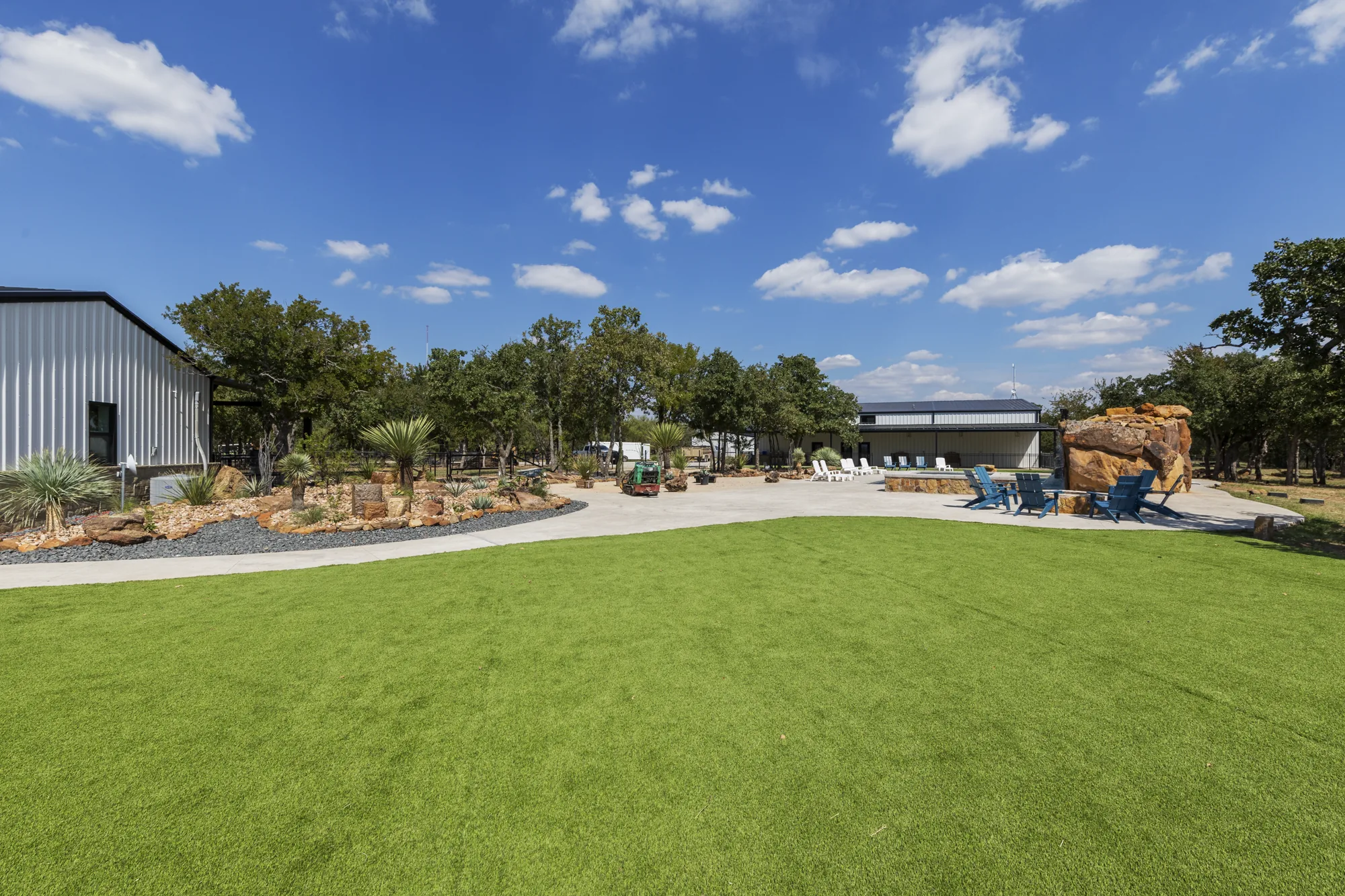 A metal barndominium with an artificial turf lawn and xeriscape beds in decomposed granite