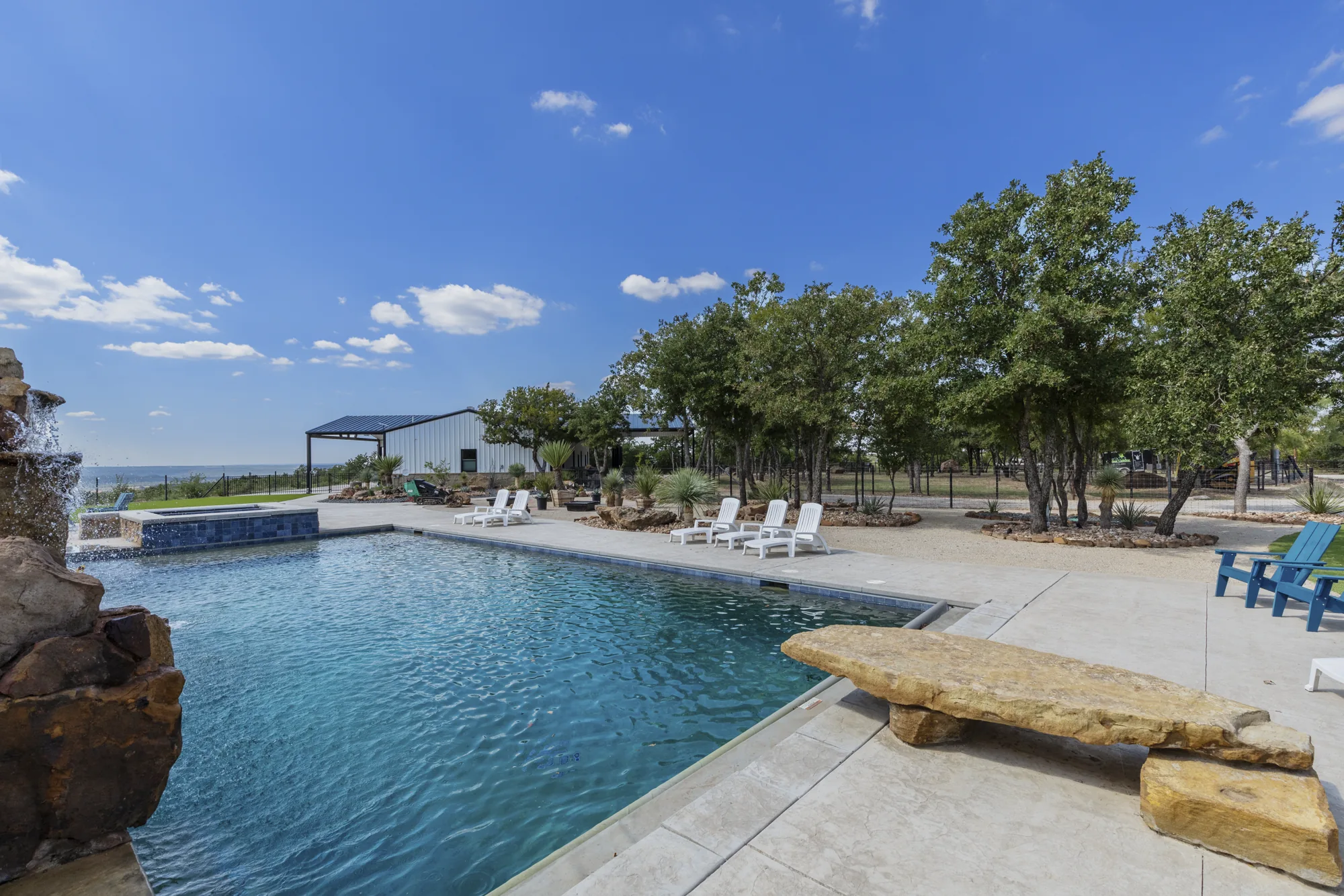A pool terrace with a cut stone slab bench and loungers, open to the hills