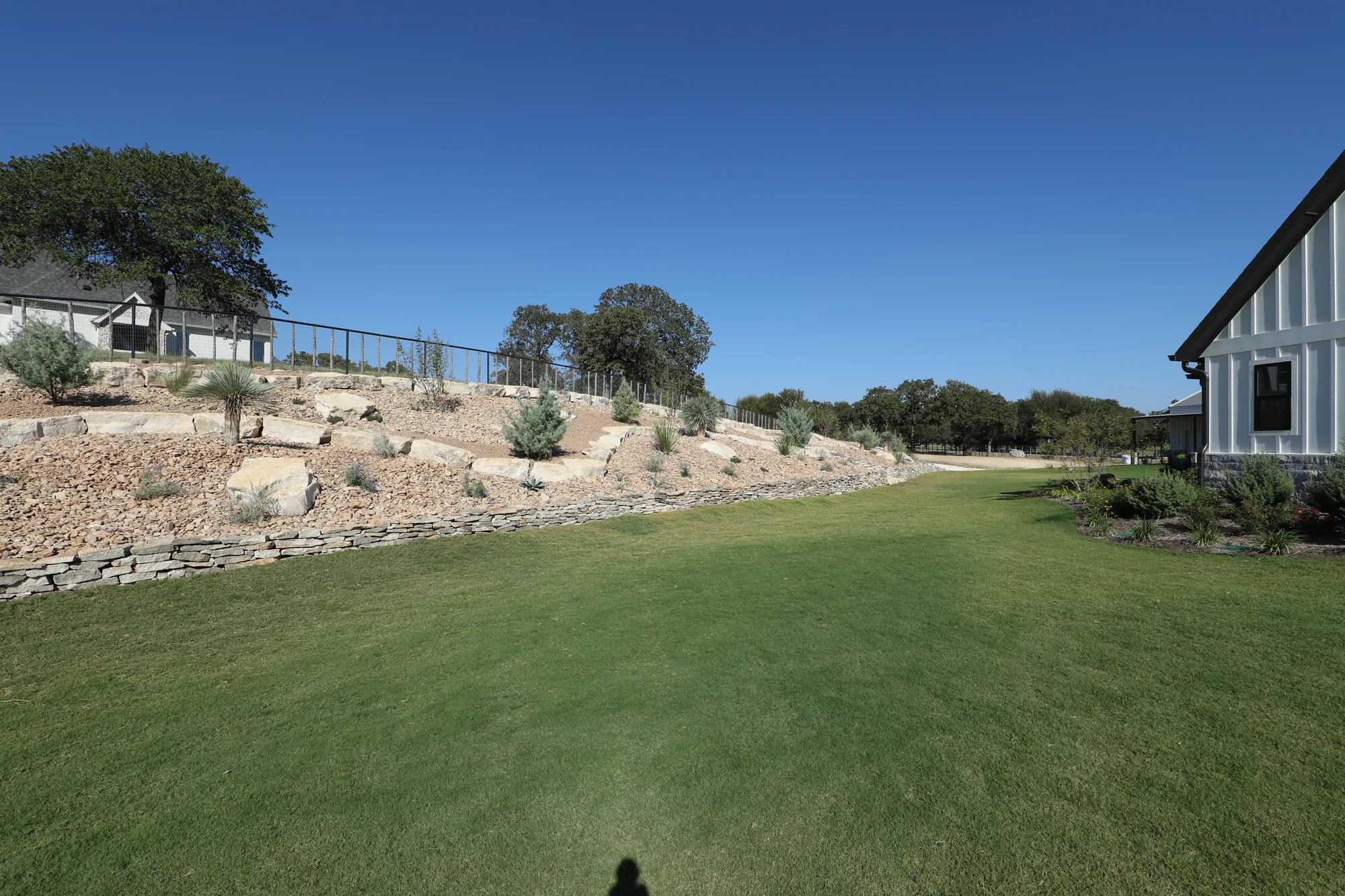 Dry-stacked limestone terraces holding a slope above a turf lawn at a ranch home