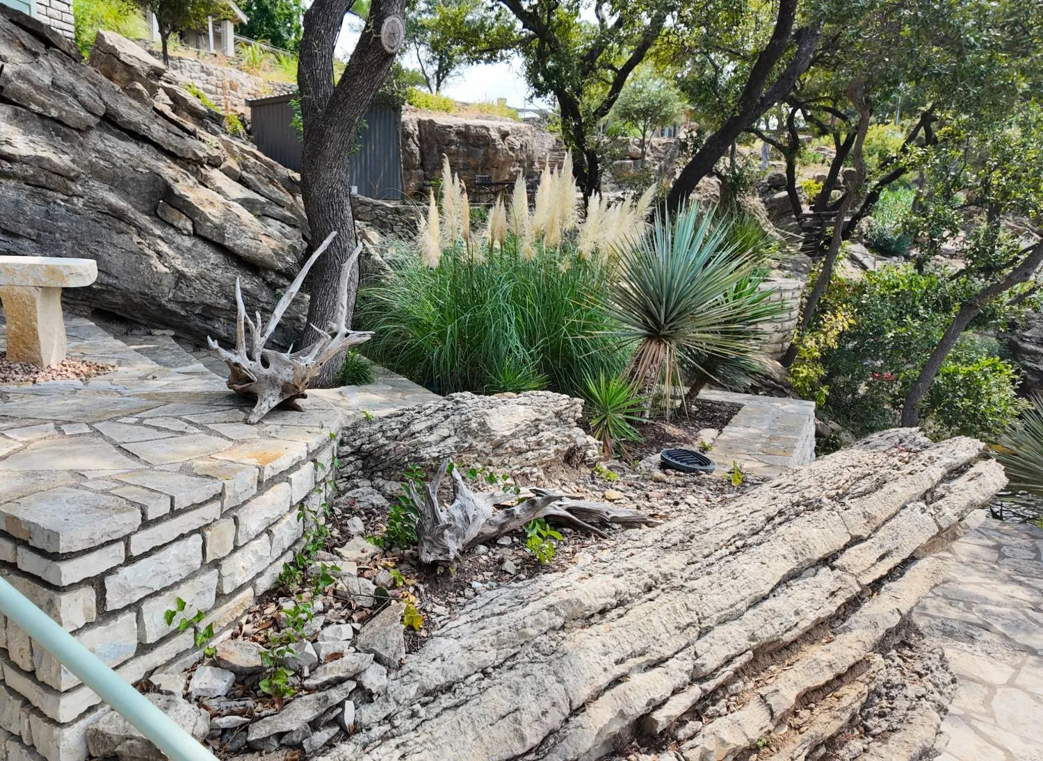 A flagstone terrace and dry-stacked limestone wall built into a bedded limestone outcrop, with pampas grass and yucca above