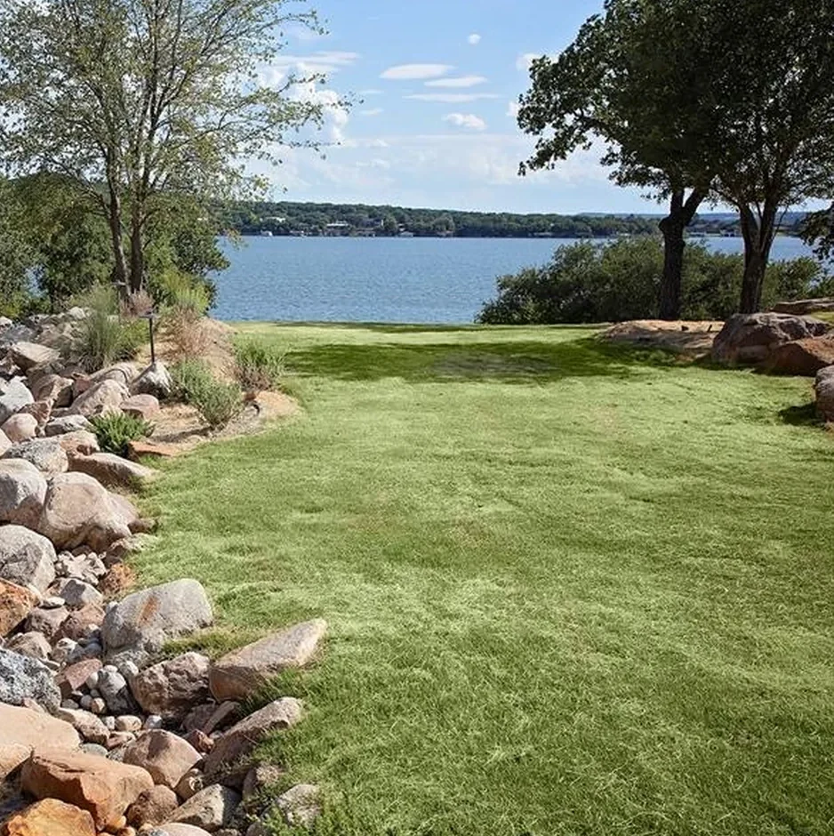 An irrigated lawn running down to Possum Kingdom Lake between boulder edging and mature shade trees