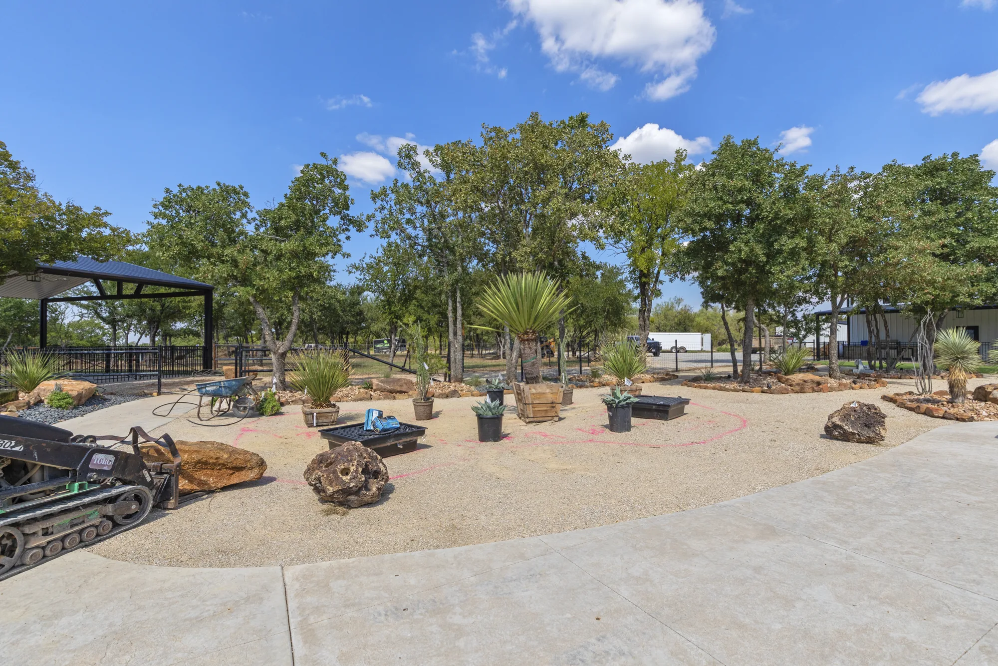 A decomposed granite yard mid-installation with a tracked loader, set boulders and new planting beds