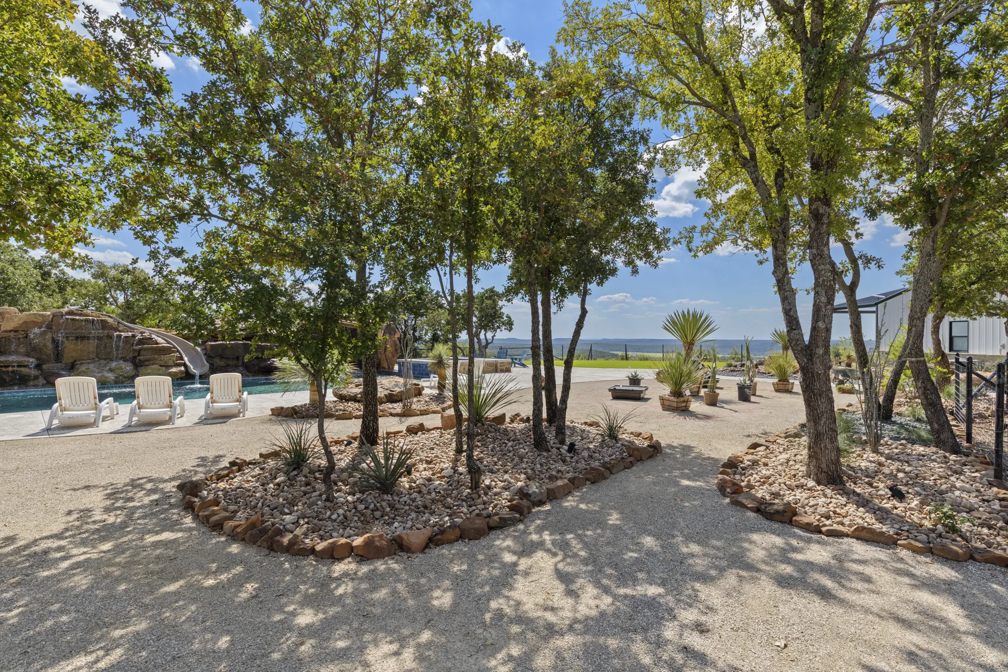 Live oaks with boulder-edged beds and decomposed granite, the pool terrace beyond