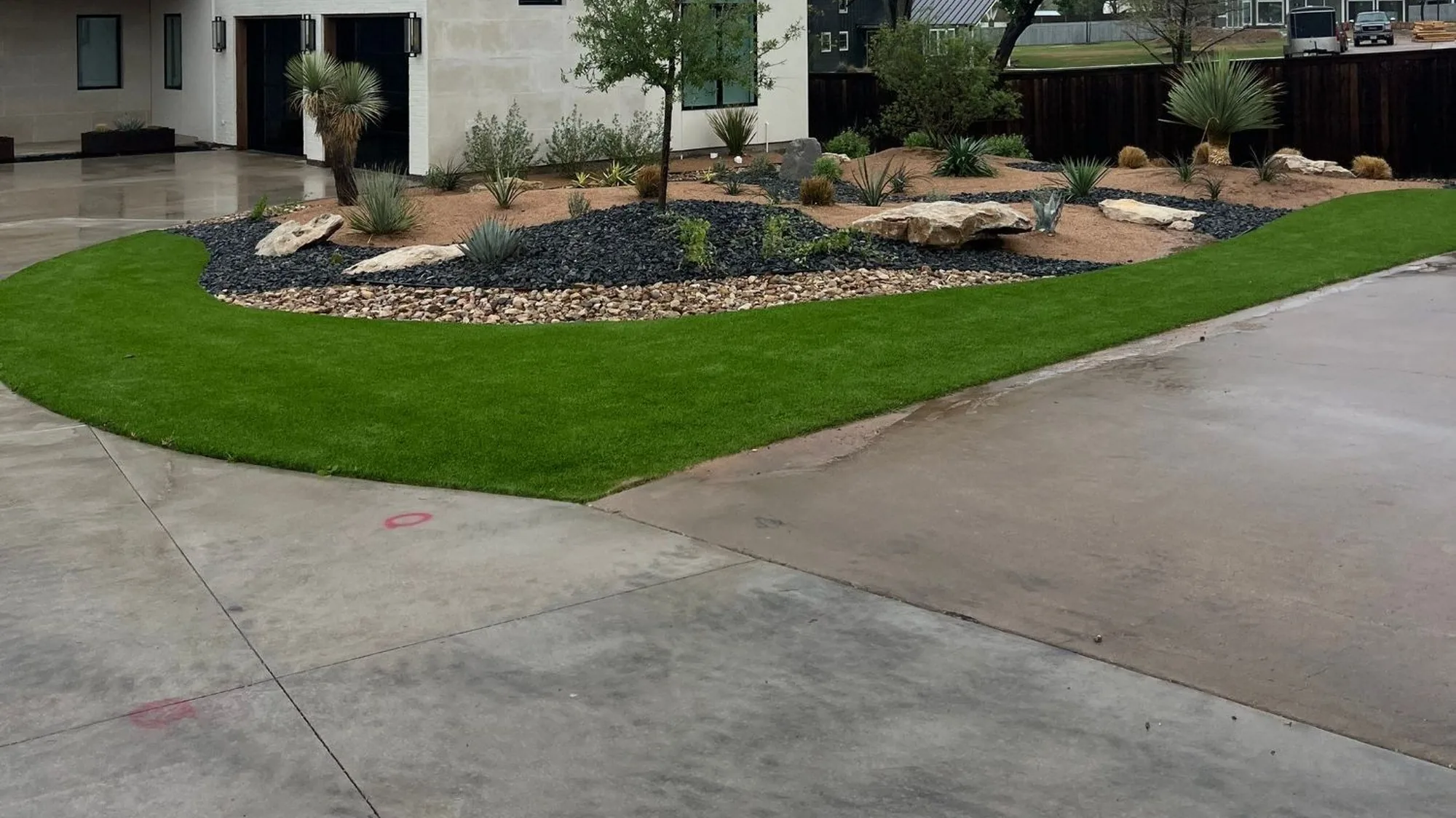 Modern home with a curved synthetic turf lawn edged against black rock and decomposed granite beds planted with yucca