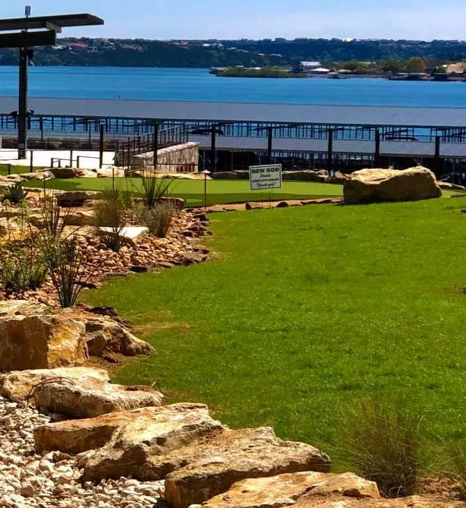 Newly laid sod establishing behind a keep-off sign, with a putting green, the lake and boat docks beyond