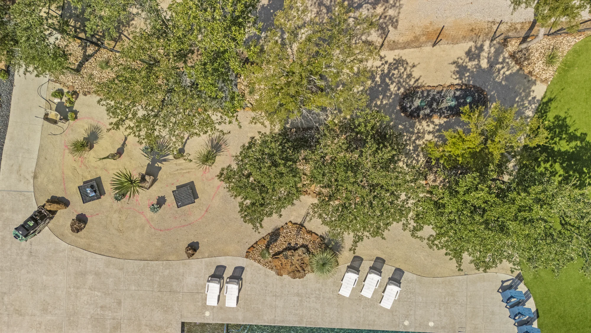 Aerial view down through a live oak canopy onto boulder-edged beds and the pool terrace