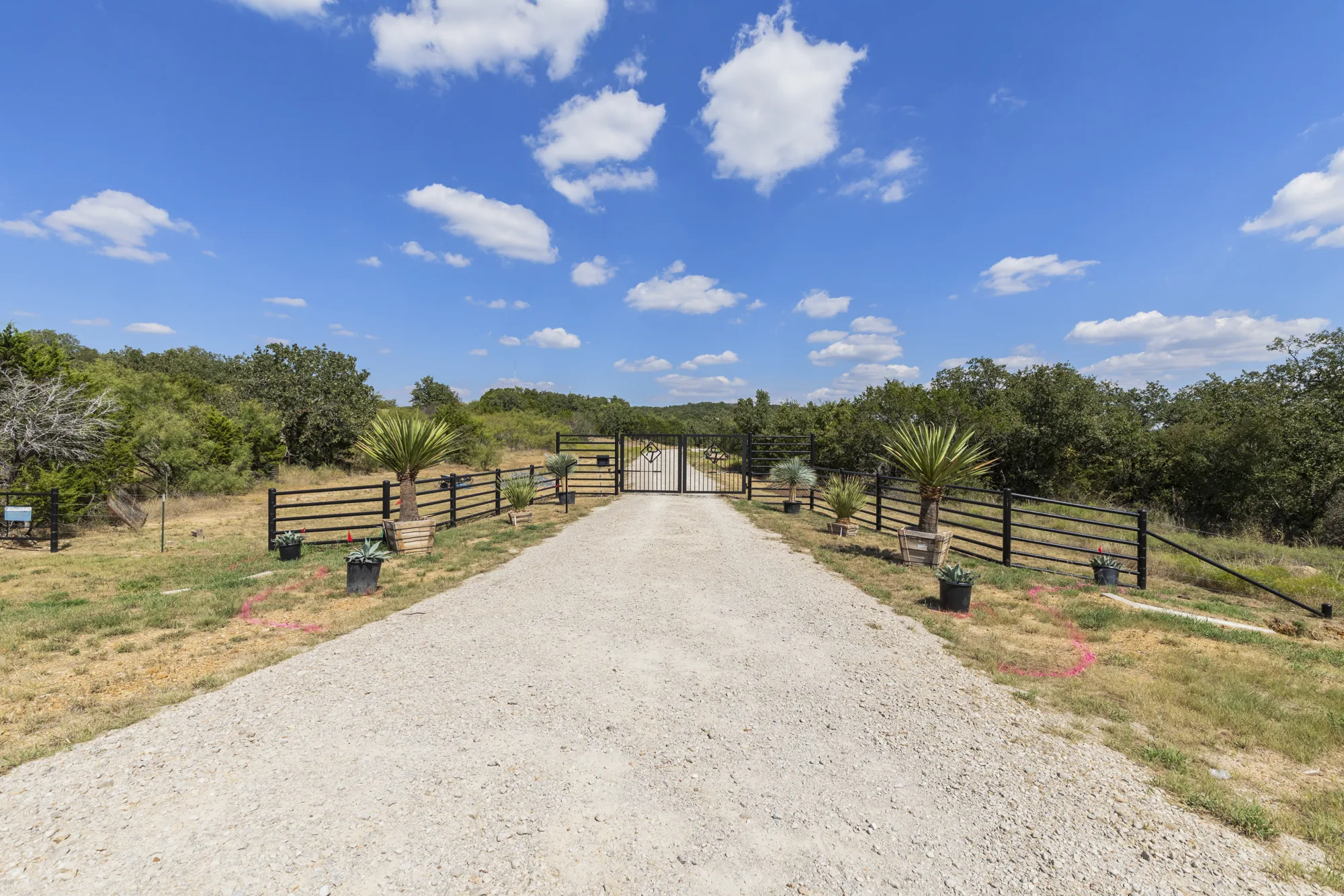 A gravel ranch drive running to a black pipe entrance gate between cedar fence lines