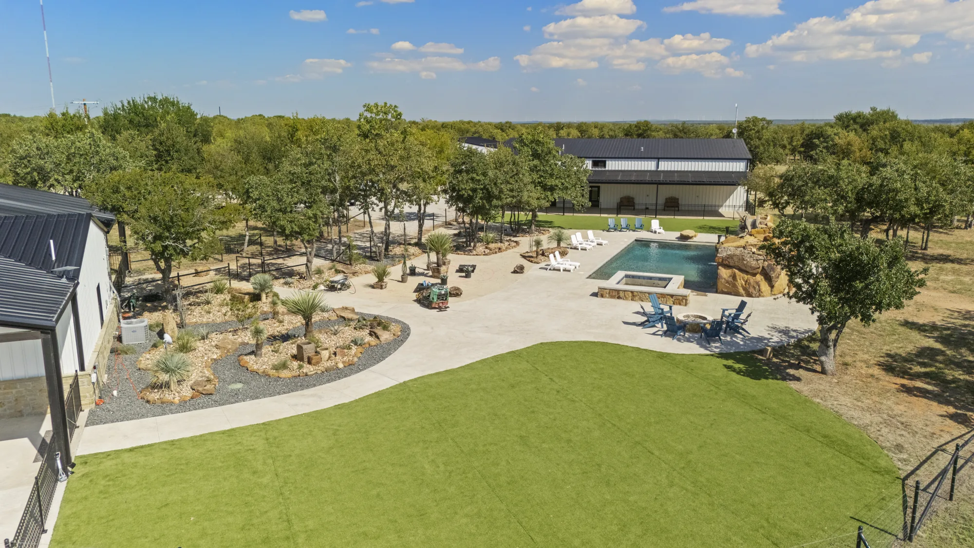 Aerial view of a ranch landscape with artificial turf lawn, pool, barndominium and mature live oaks