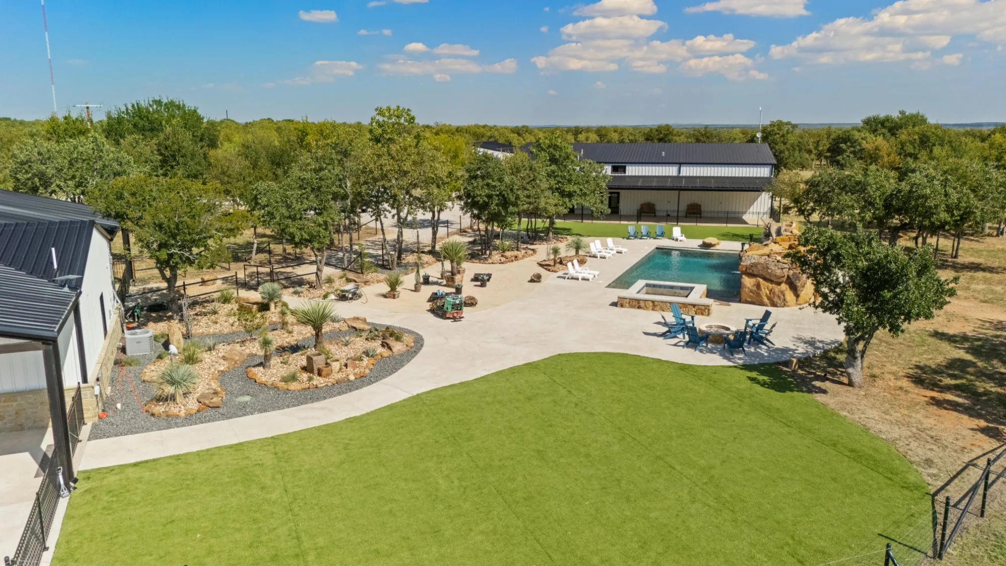 Aerial view of a turf lawn, pool and rock water feature around a hillside home
