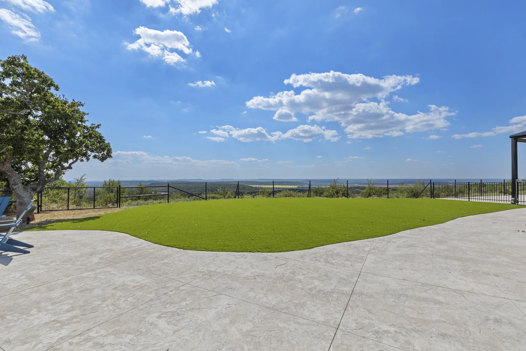 Artificial turf lawn meeting a broom-finish concrete edge, with black ranch fence and the hills beyond