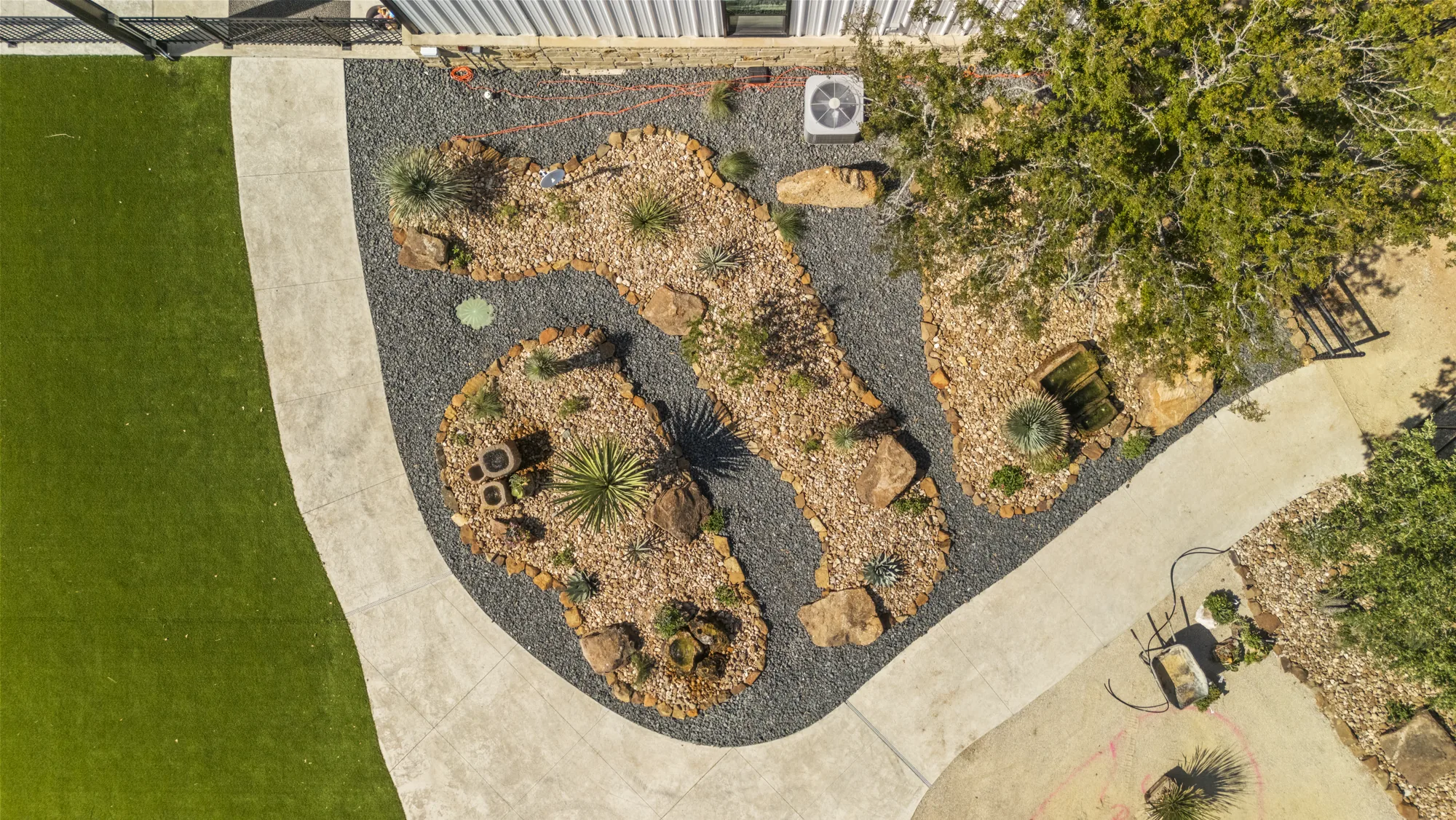 Overhead view of a turf lawn meeting a boulder and rock mulch planting island