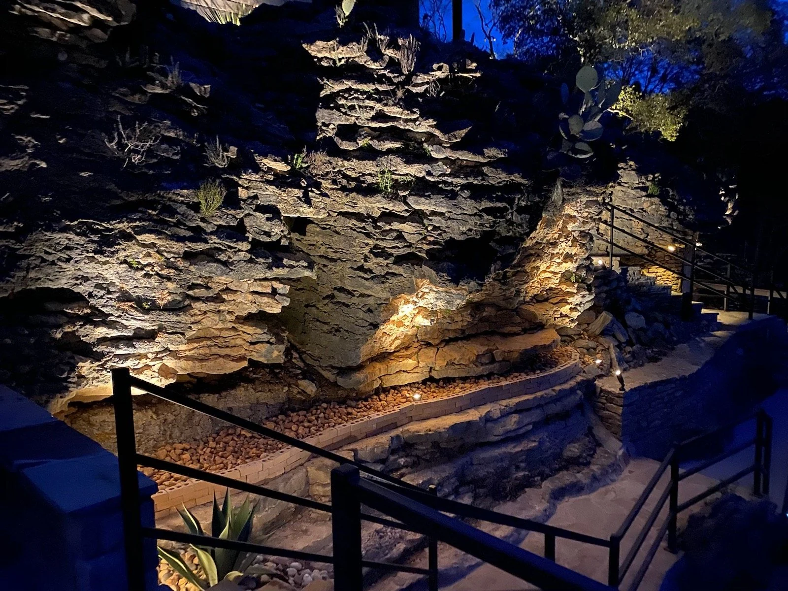 A natural stone hillside terraced with steps and uplighting, above a dry creek bed at twilight