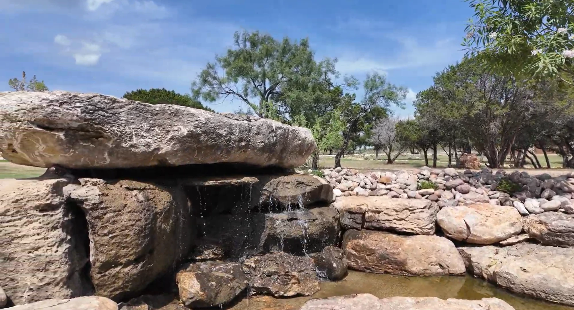 Water sheeting from beneath a broad limestone capstone into a shallow pool set in a river rock bed