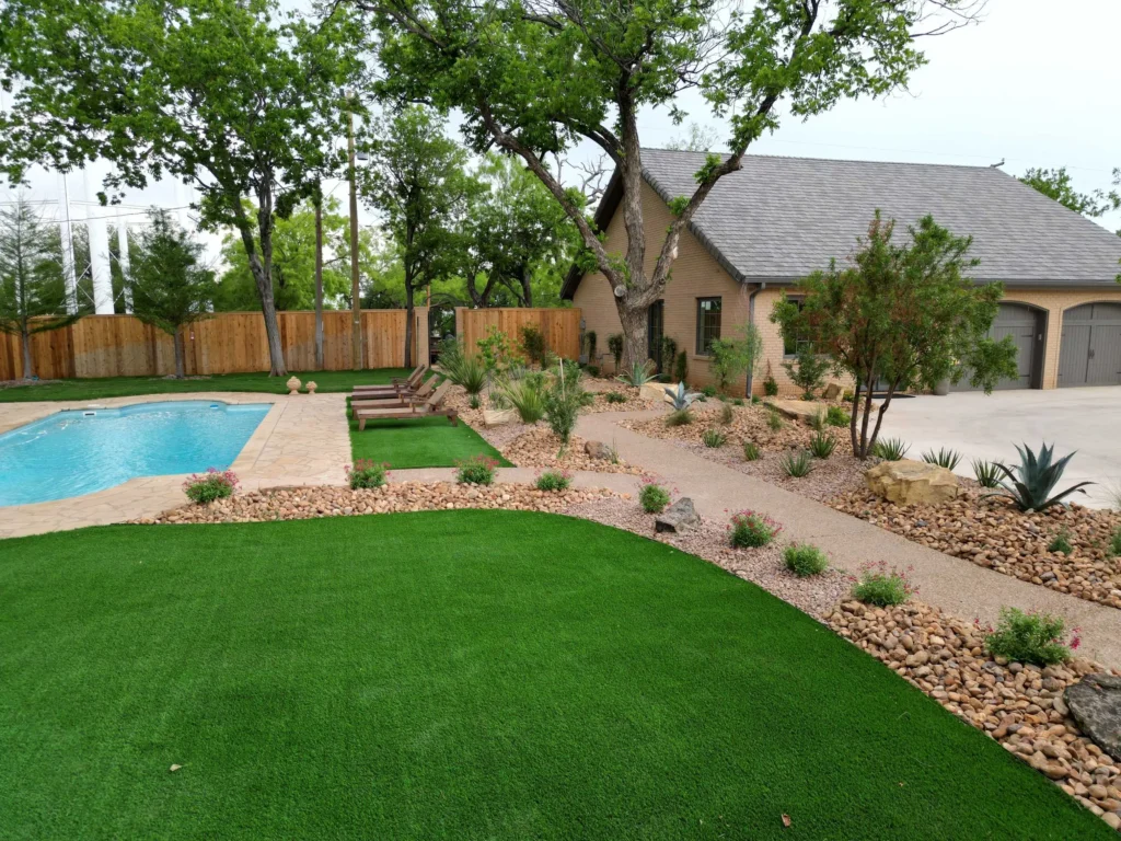 landscaped backyard with a pool, green lawn, gravel path, and surrounding trees.