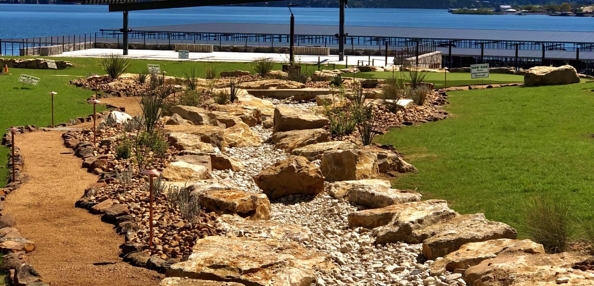 Dry creek bed landscape design featuring smooth stones, gravel, and native plants, enhancing outdoor space for drainage solutions and aesthetic appeal.