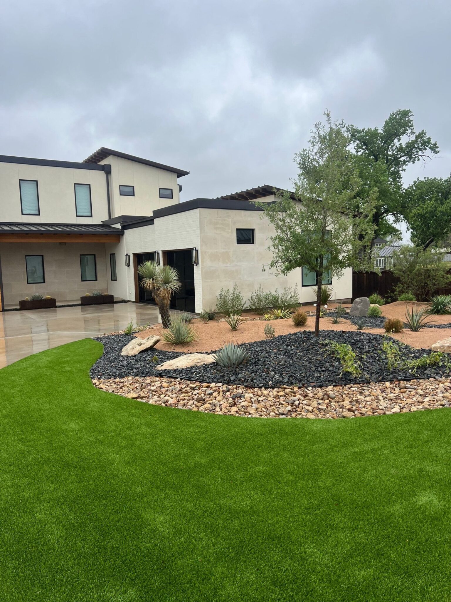 Modern home with xeriscaping, artificial turf, decorative rocks, and native plants, showcasing sustainable landscaping solutions by Let Us Do It Landscaping LLC.