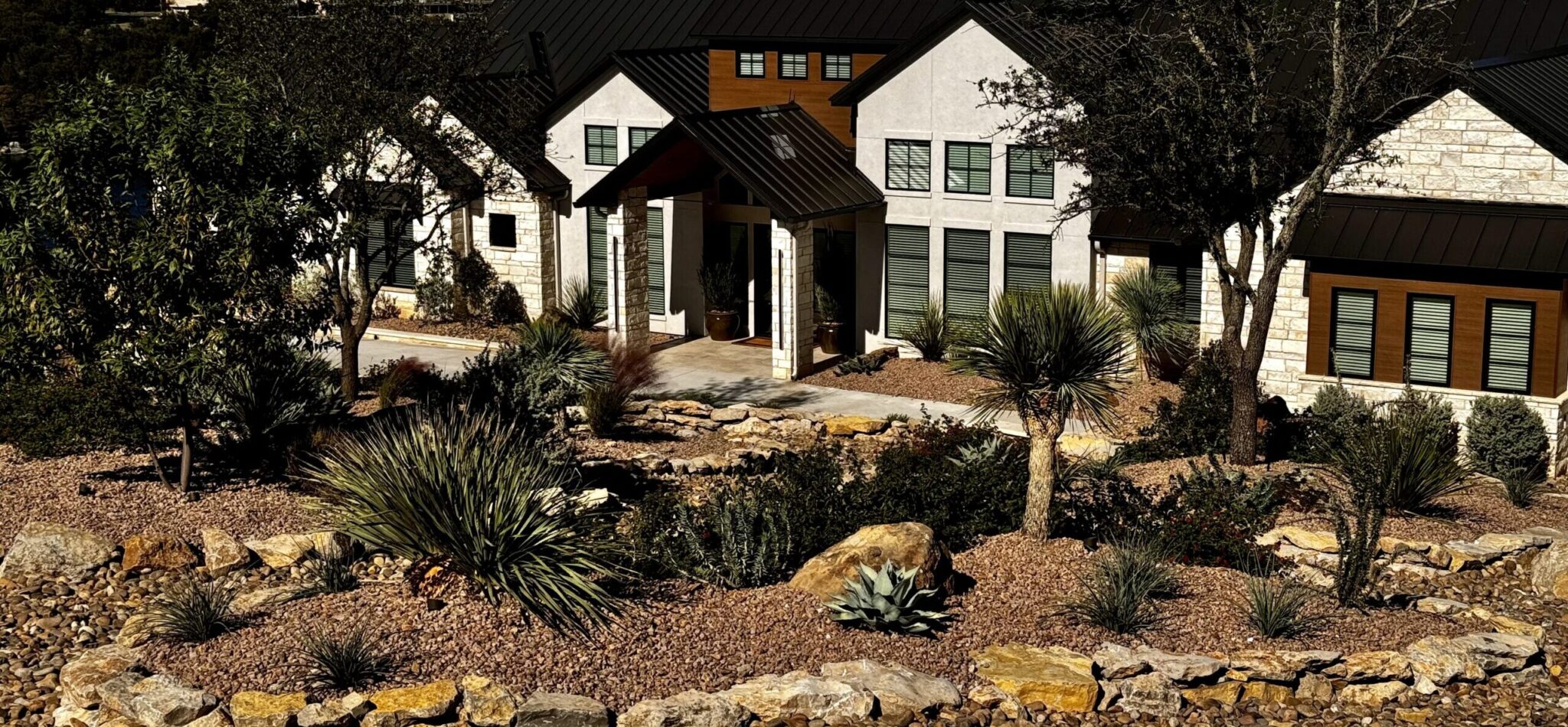 Xeriscaped front yard featuring native plants, decorative rocks, and a modern home entrance, illustrating sustainable landscaping solutions by Let Us Do It Landscaping LLC.